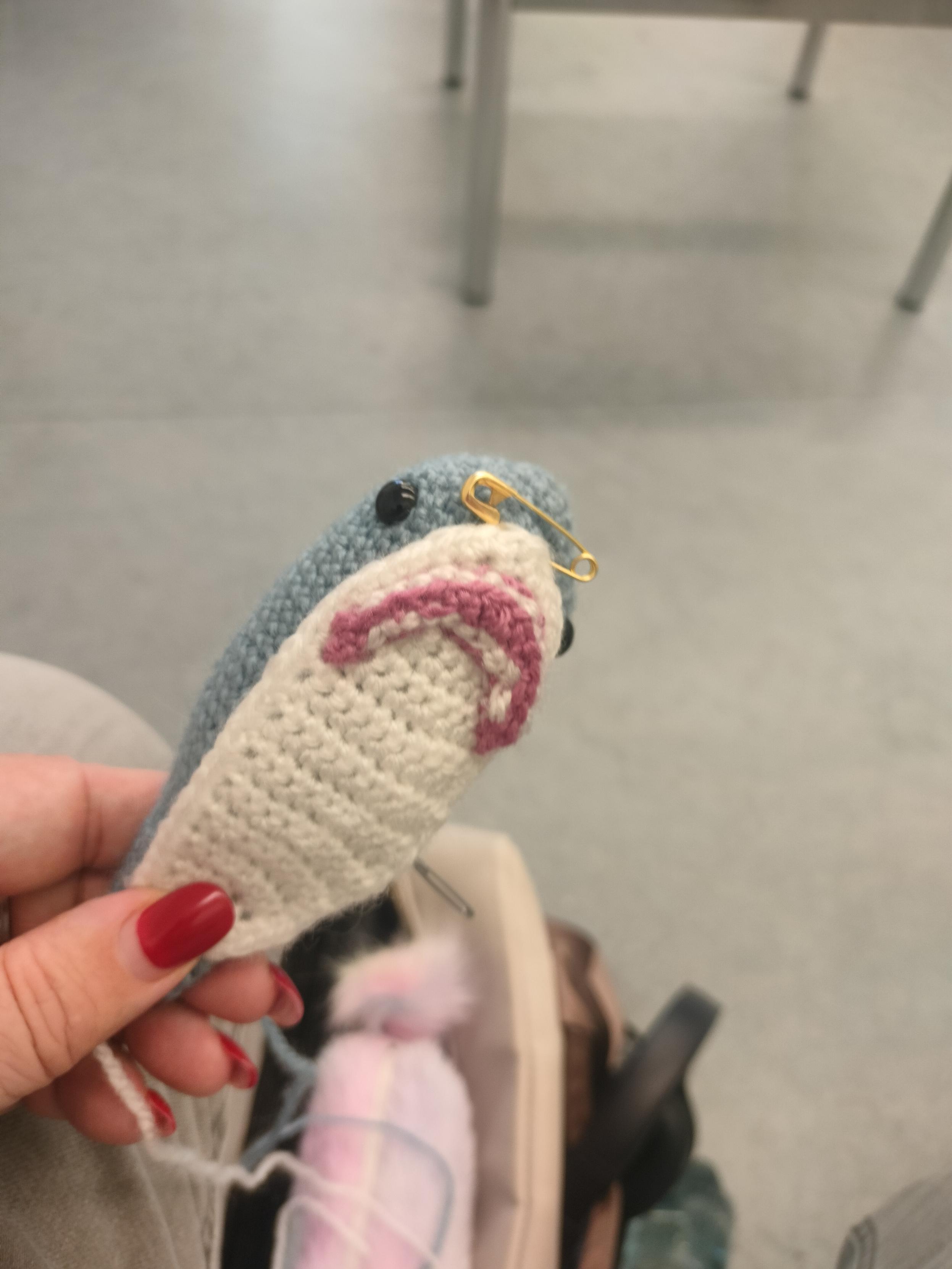 A crocheted Blåhaj body with with a white belly and somewhat mangled mouth pinned on